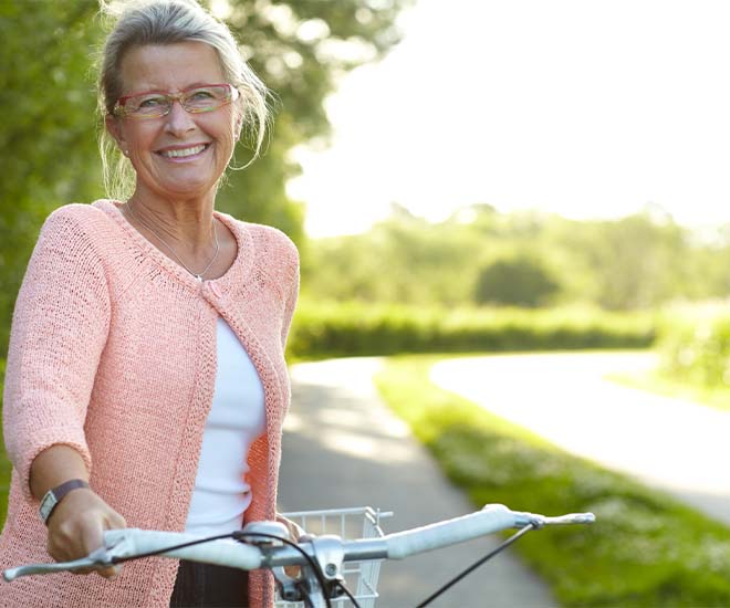 Woman in a pink sweater with a bike in a park