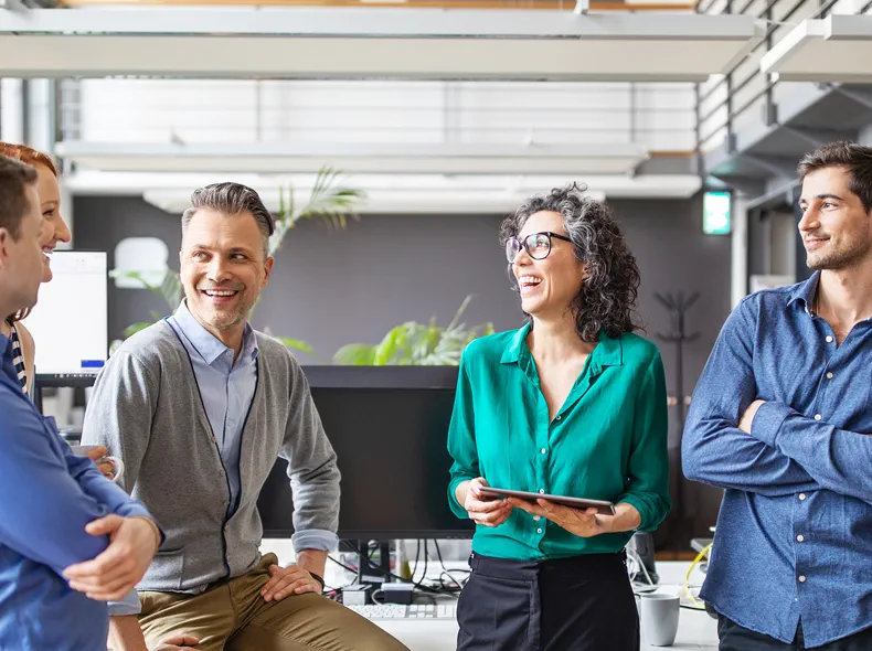 A group of coworkers in an office, standing in a circle and laughing