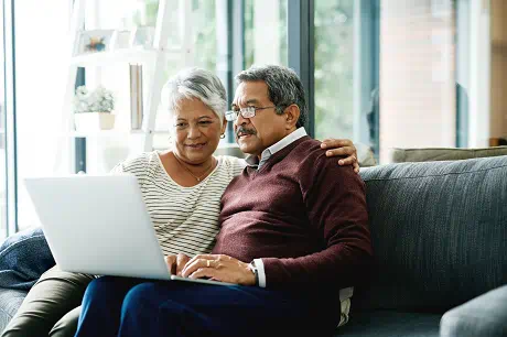 An elderly couple sits on a couch, looking at a laptop