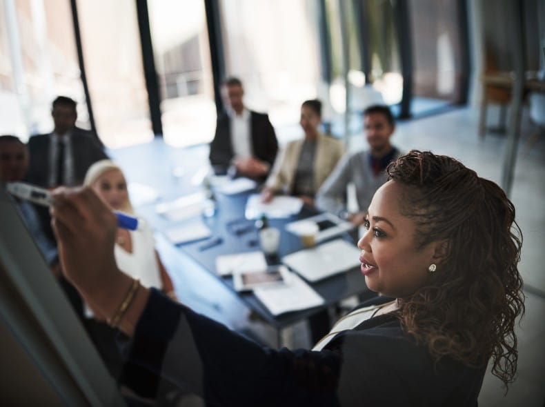 an image of a women writing on a whiteboard during a meeting.