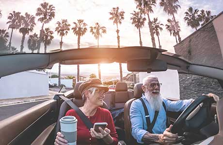 two elderly people driving in a convertible along the beach