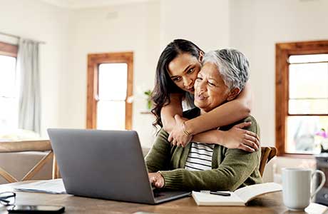 a younger woman hugging an older woman while looking at a laptop screen