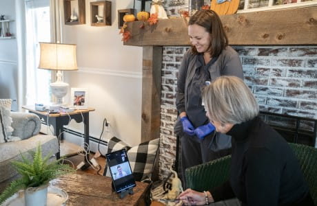 a older woman talking to a doctor over an ipad screen from her home with a nurse standing near