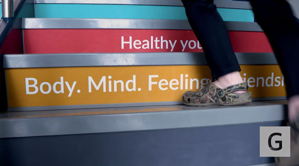 A person wearing sandals walks up colorful steps labeled "Body. Mind. Feelings. Friends." and "Healthy you."