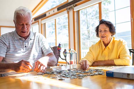 Image if Ms. Bennick with he husband doing a puzzle in their sunny living room