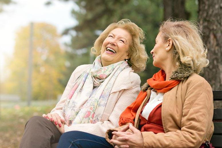 two aging women laughing on a park bench
