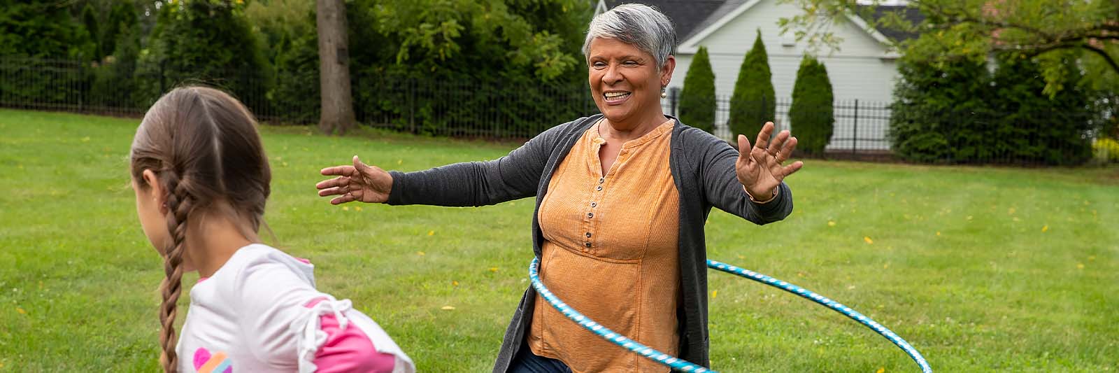 Grandmother hoola hoops with her granddaughter in the backyard.