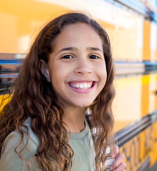young girl smiling near school bus