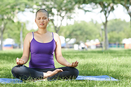girl with shaved head meditating in the park