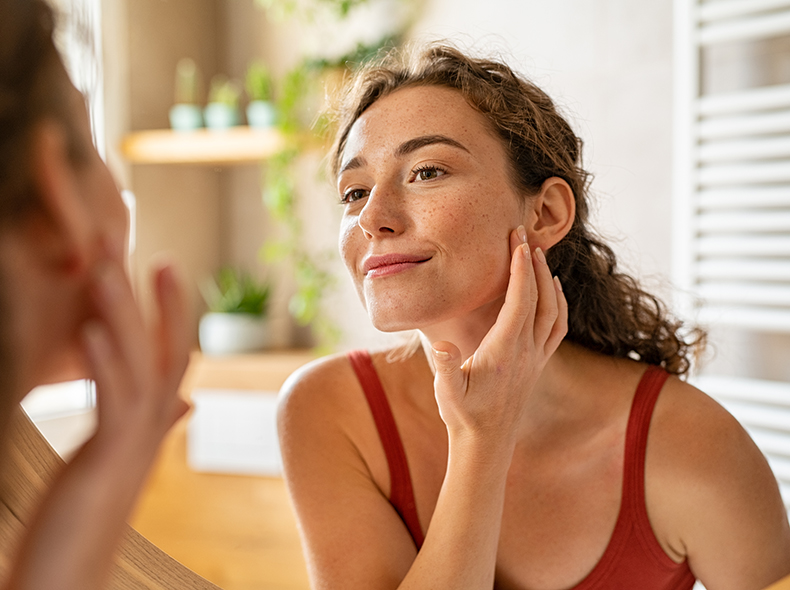 A young happy woman looks at her skin in the mirror and is pleased with what she sees.