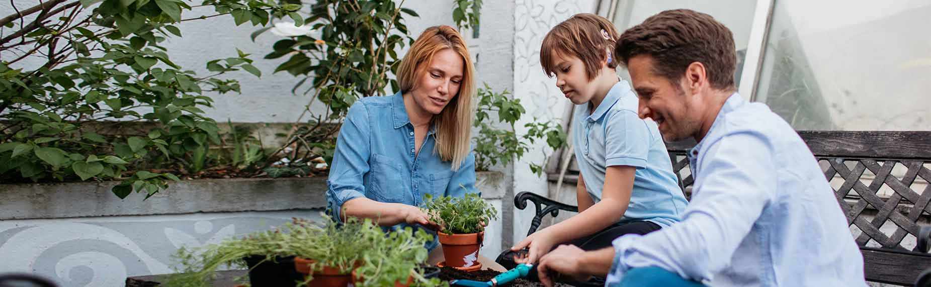 Father, mother, and their son with cochlear implant planting herbs on balcony.