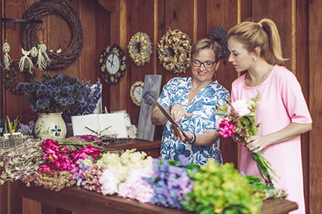 Tow women working together at a flower shop one lady is wearing glasses. 