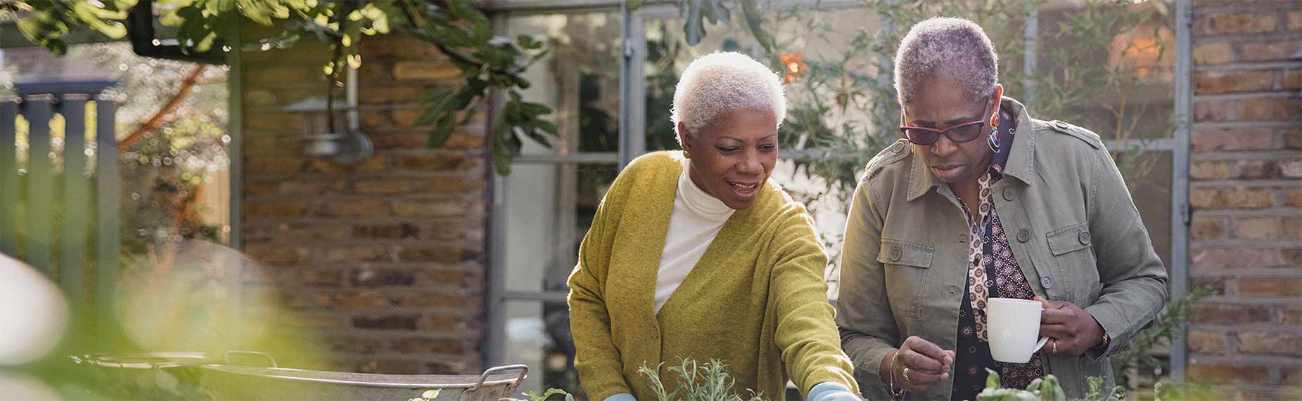 Two mature women in a garden chatting and catching up while one of them does gardening work.