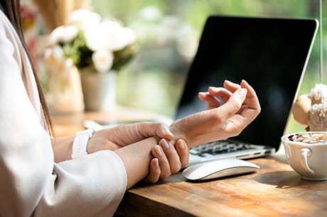 an image of a woman holding her wrist in front of a laptop