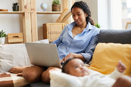 New mother on computer with newborn near her side