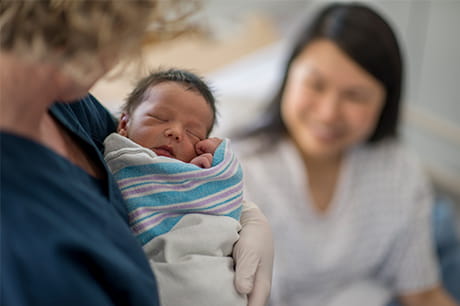 new mother staring up at newborn while nurse is holing the infant