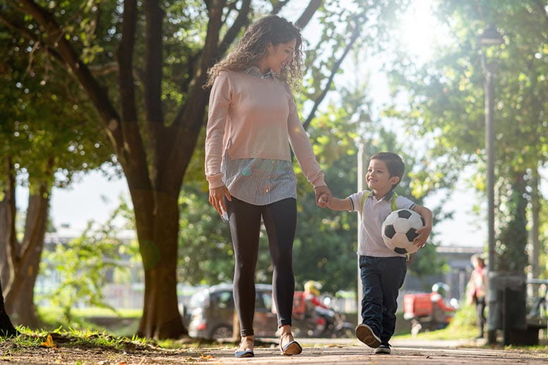 Mother and son walking down street with soccer ball