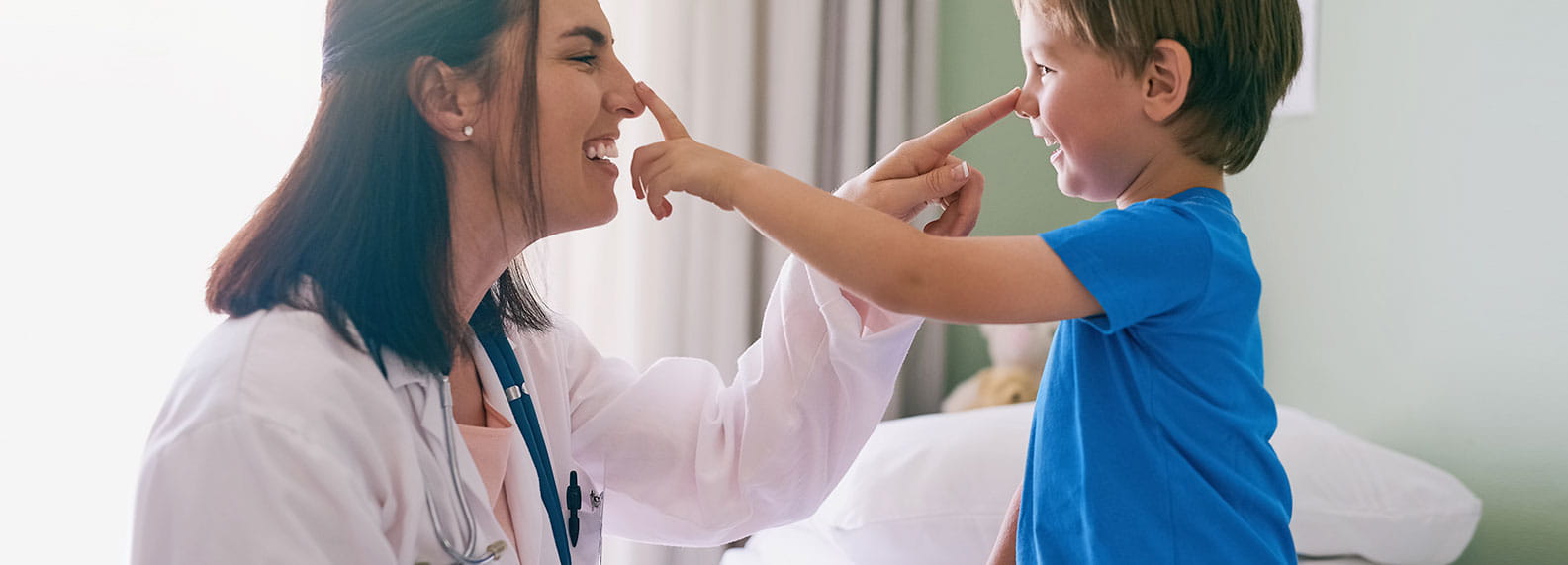Pediatrician and toddler playfully touching each other’s noses.