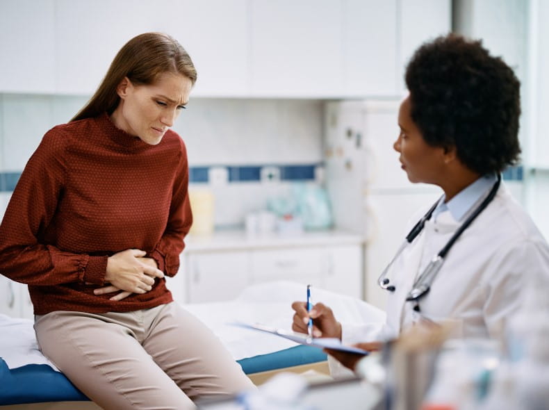 Woman holding stomach while talking to doctor.