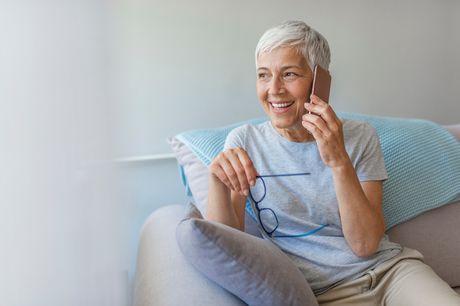 Senior woman sitting on the couch at home, talking on her phone.