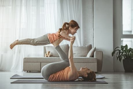 Woman on a yoga mat in a living room lifting her child. 