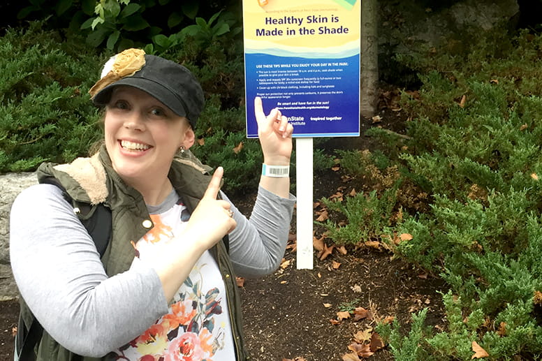 Woman pointing at sign outdoors that says healthy skin is made in the shade