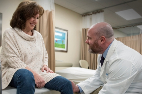 Orthopedic surgeon Dr. James Murphy examines Chery Bednar for her one-year checkup after having total lifetime hip replacement surgery. Cheryl sits on exam table while Dr. Murphy lifts her foot to test her hip joint.