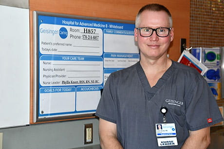 John, a cardiac nurse, stands in the hospital near a patient board.