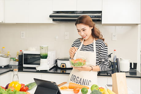 A woman reviews a recipe on a digital device in a kitchen.