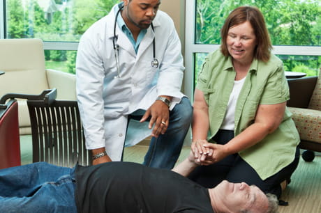 Doctor and woman leaning over a man on the floor.