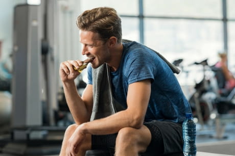 Man eating protein bar at the gym