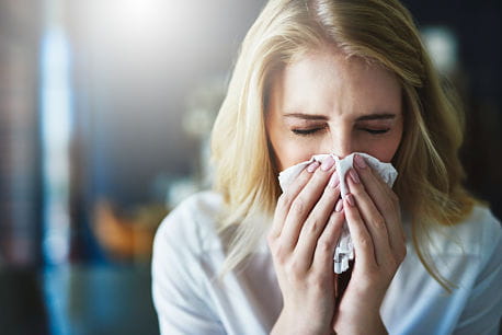 Sick woman with cold or flu blowing nose