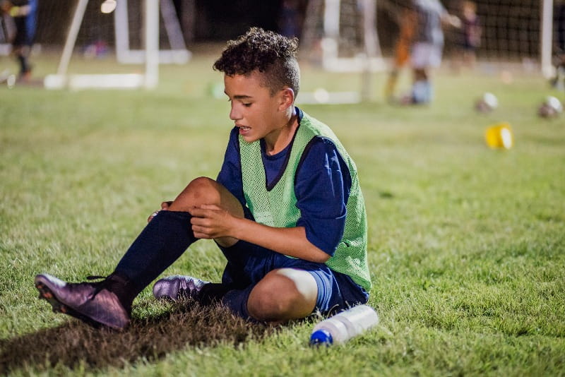 Injured child holding shin while sitting on soccer field.