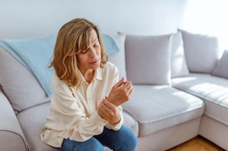 Woman sitting on couch experiencing carpal tunnel wrist pain.