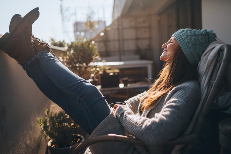 A young woman in a knit hat sits in the sun with her feet up, to help combat seasonal affective disorder.