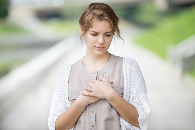 Woman with worried look on her face clutches her chest with AFib symptoms.