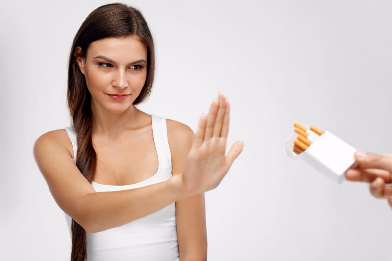 Young woman sticking her hand out to say ‘no’ to a pack of cigarettes
