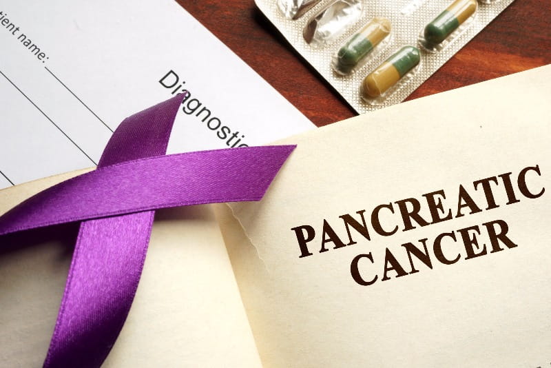Notepad that says pancreatic cancer next to a purple ribbon.