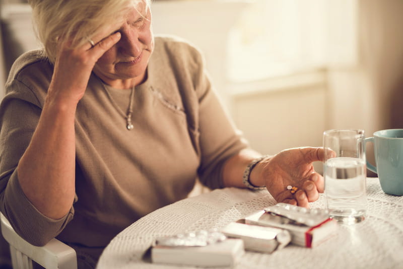 Older woman holding her head in her hand while about to take pain medication.