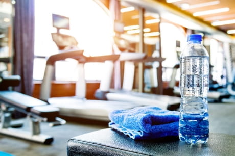 Water bottle and blue towel on a workout bench in an empty gym.