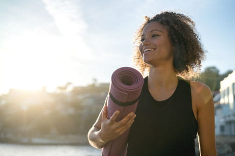 Young, happy woman outside with a yoga mat.