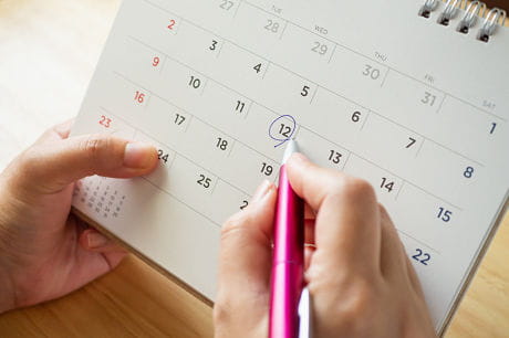 Female holding calendar, circling date when her ovulation cycle starts.
