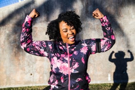 Woman in bright athletic jacket flexing arms after exercising.