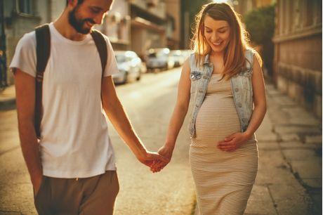 Pregnant woman walking and holding hands with man on a street. 