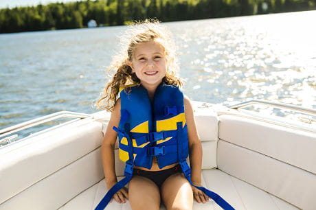 Little girl wearing a life jacket in a boat on the lake.