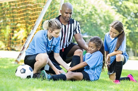 Soccer coach and referee tending a female player's injury