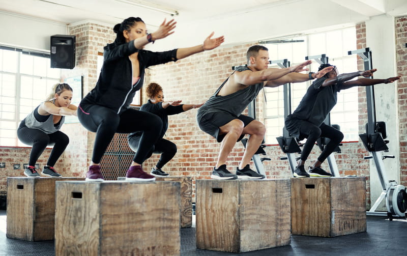 Shot of a focused group of young people jumping onto crates as exercise inside of a gym