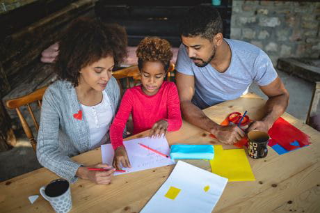 Parents sitting at a table and helping their child with homework.