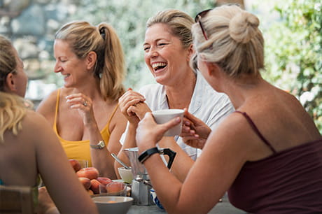 A group of middle-age women, laughing together at an outdoor cafe.