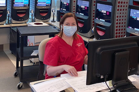 Mary Ann Heller sits in front of the machines first used to test Geisinger patients for COVID-19